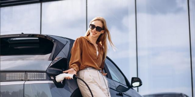 Frau beim Laden an einem Elektrofahrzeug gelehnt