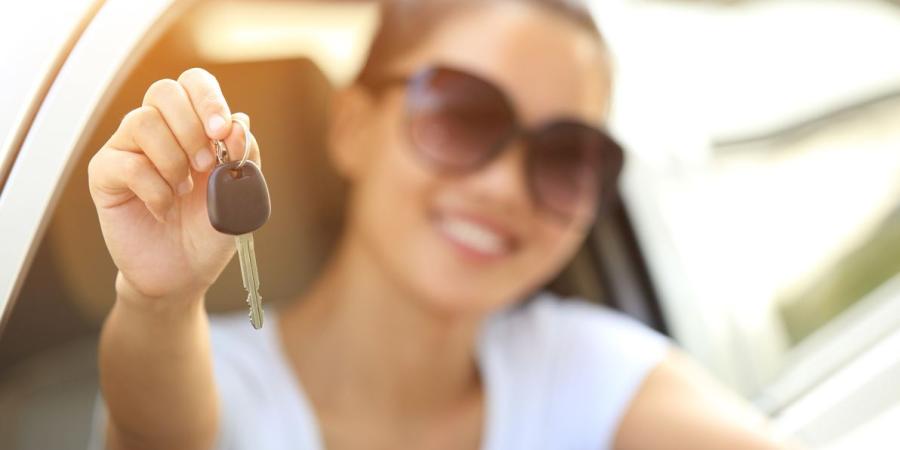 Junge Frau mit Sonnenbrille im Auto hält Autoschlüssel in die Kamera - Flexible Leasingoptionen nutzen
