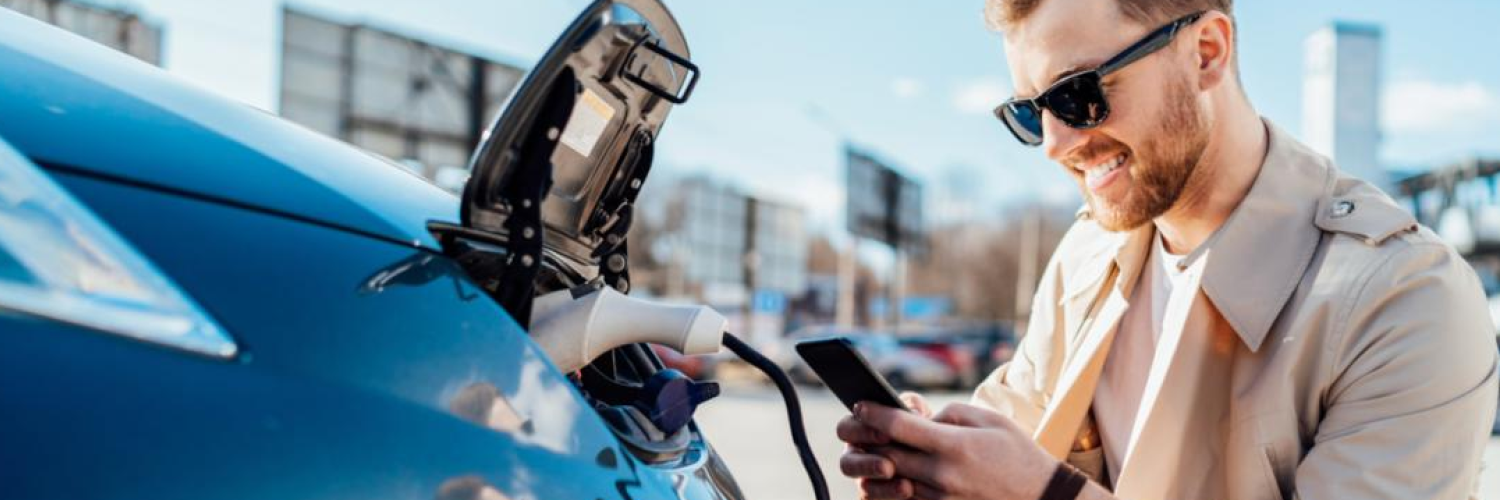 Mann mit Handy und Sonnenbrille beim Laden seines Elektroautos als Symbol für effizientes Fuhrparkmanagement