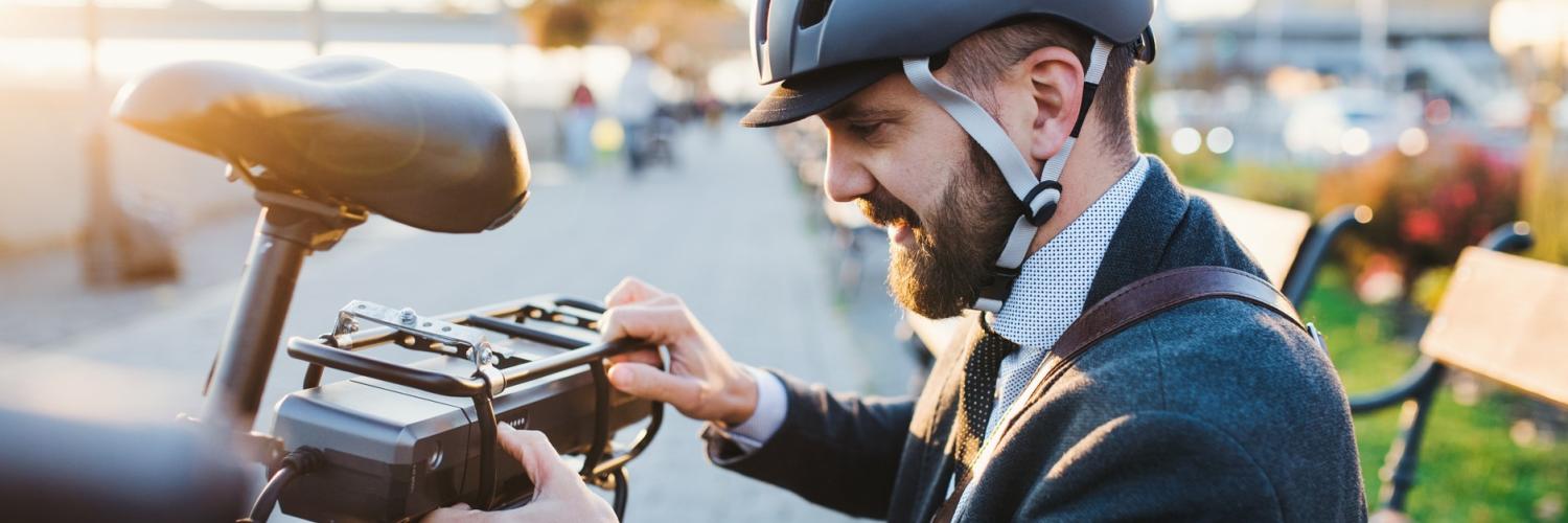 Bike Leasing-Mann mit Helm vor seinem Akku Mann mit Fahrradhelm ist am Akku seines Elektro-Dienstrads zu Gange als Symbol für Mobilitätslösung für Mitarbeitende