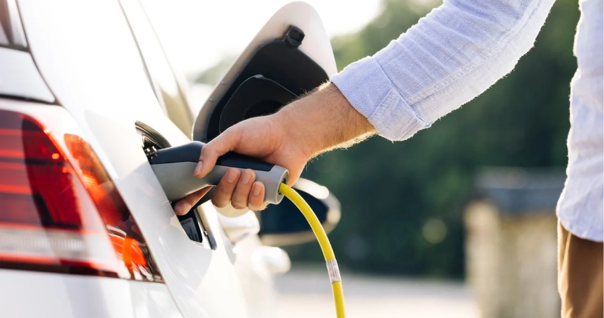 Person steht neben E-Auto und hält Ladestecker in der Hand - Lesen Sie nützliche Hinweise und Tipps rund um Elektrofahrzeuge