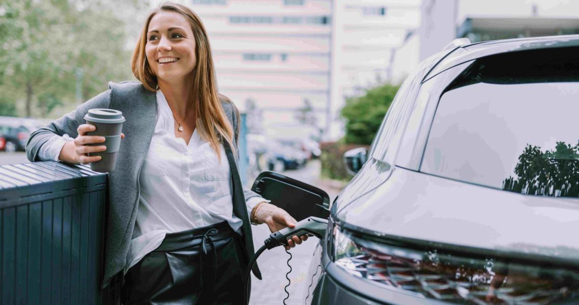 Arval Mittelstand-Frau mit Kaffee beim Ladevorgang Frau mit Kaffee to go in der Hand beim Laden ihres Elektrofahrzeuges nutzt die flexible Langzeitmiete von Arval