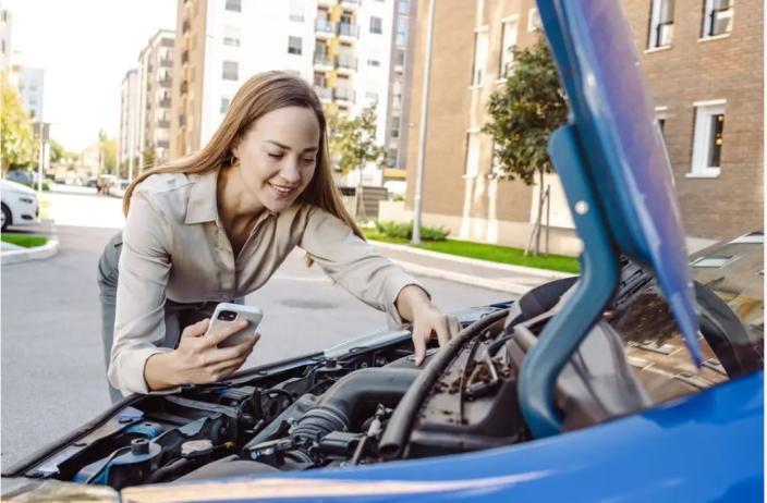 Junge Frau steht vor Motorhaube und beschreibt per Telefon eine Panne - Melden Sie Ihren Schaden per Hotline an Arval