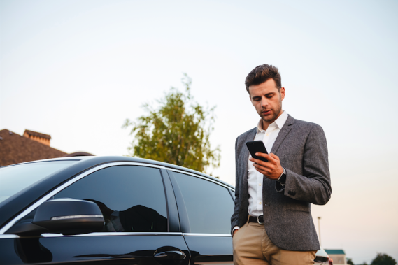 Mann steht neben Auto und meldet Autopanne via Handy  - Melden Sie Schäden bequem online oder über die My Arval Mobile App