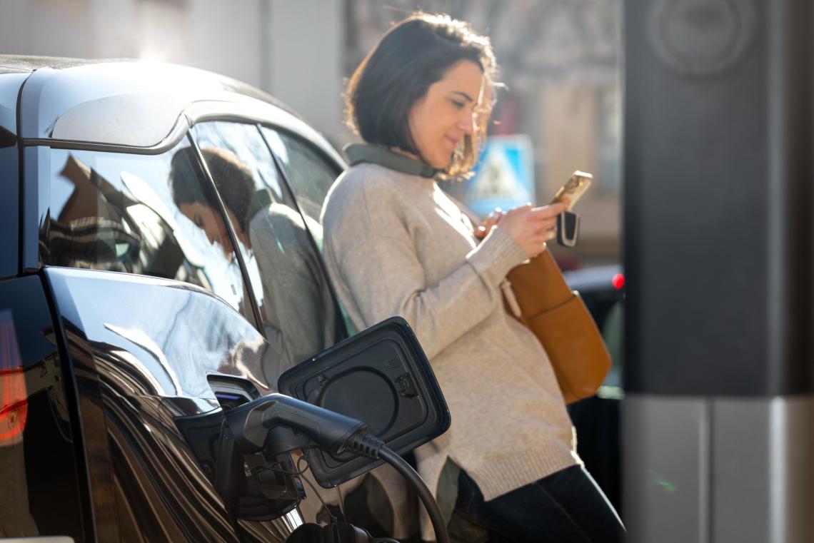 Frau mit Handy tankt ihr Auto